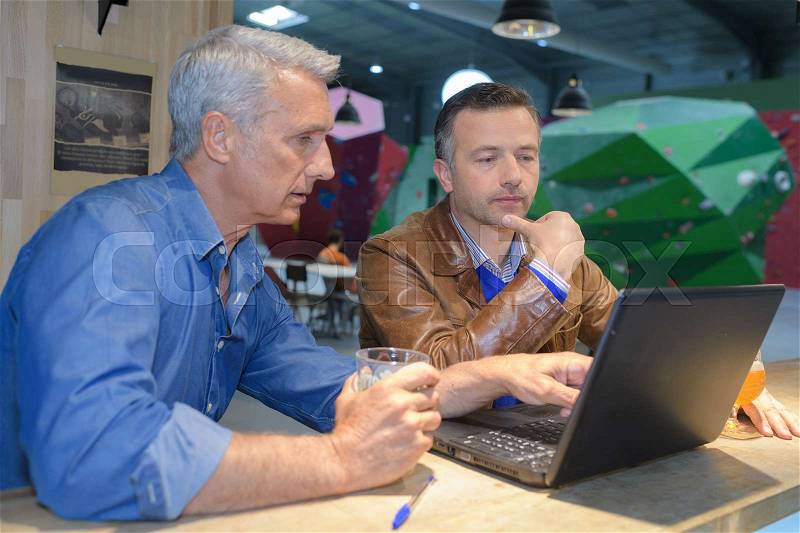 Two men using a laptop in a cafe bar, stock photo