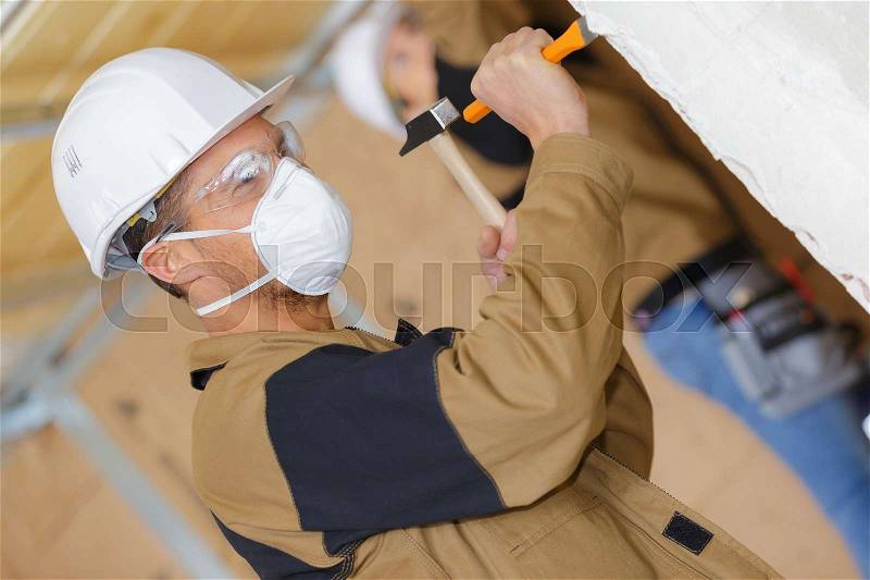 Construction worker demolishing old wall with chisel and hammer, stock photo