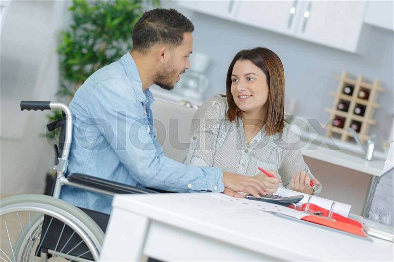 Happy wife eating at home with her disabled husband, stock photo