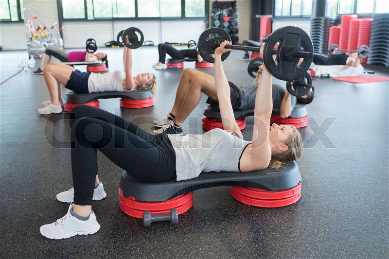 People exercising with weights at gym club, stock photo