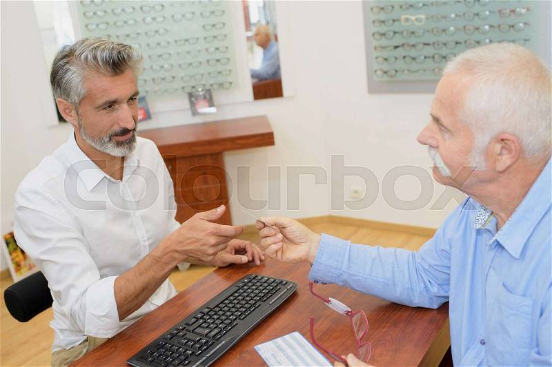 Professional male optician consulting senior man customer, stock photo