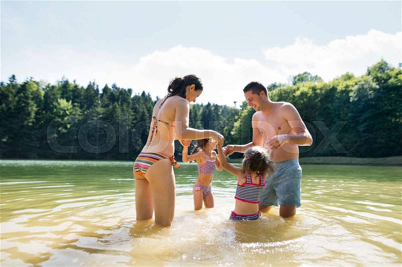 Young mother and father with their daughters in the the lake. Summer heat and water, stock photo