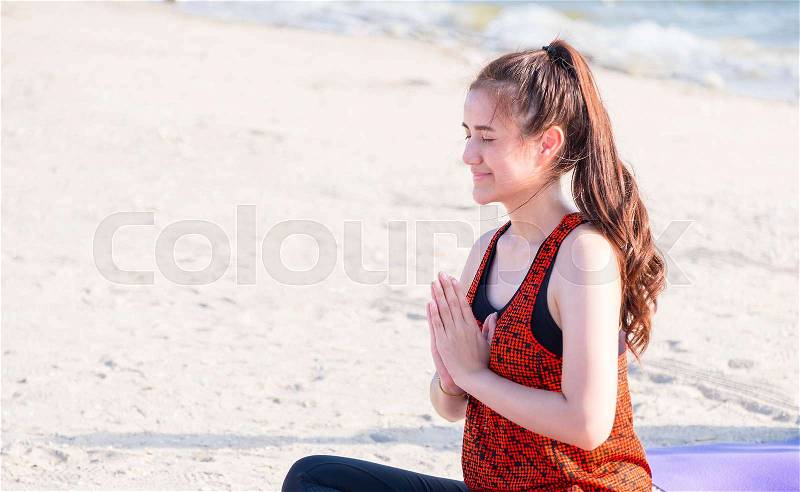 Asian woman seated doing hand namaste yoga pose on sand at coastline beach, Calm and relax concept,wellness and healthy lifestyle, stock photo