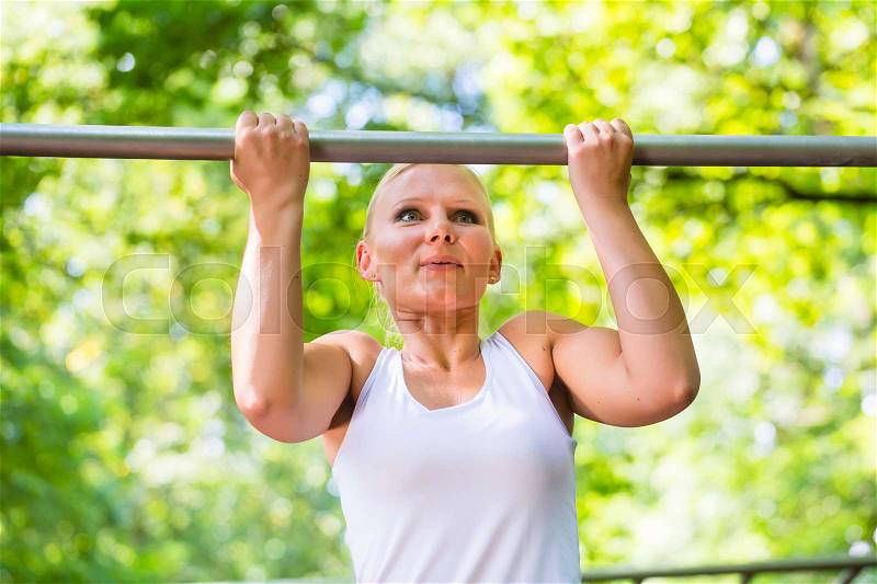 Woman exercising at high bar for better outdoor fitness in park, stock photo