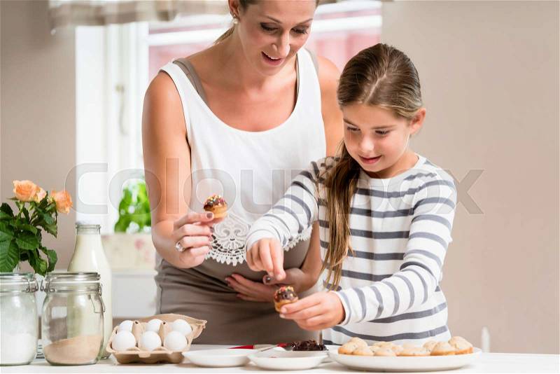 Pregnant mum and her little daughter baking together and decorating the cupcakes, stock photo