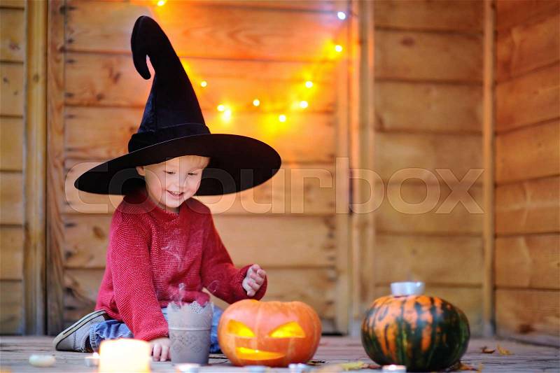 Cute little wizard with magic wand and jack-o-lanterns. Halloween decorations and lights on background, stock photo