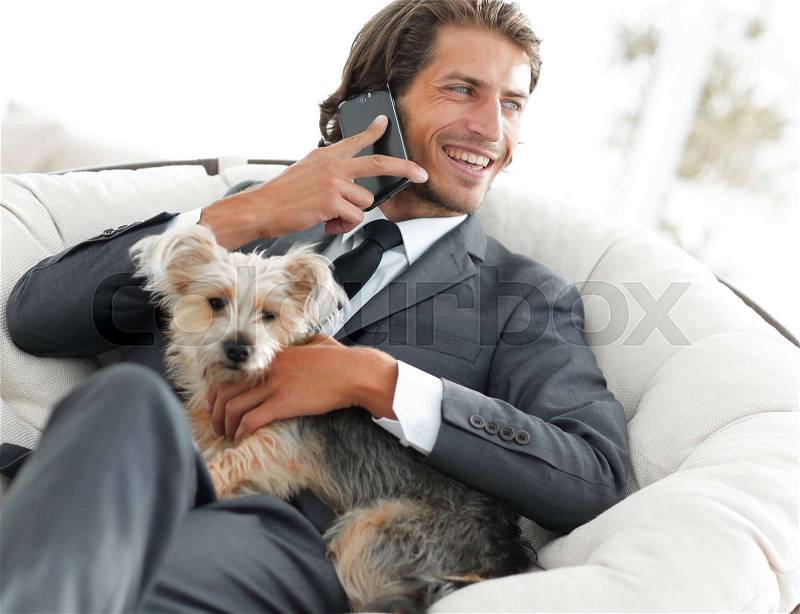 Successful businessman holds his dog and pet and talks on the smartphone, stock photo