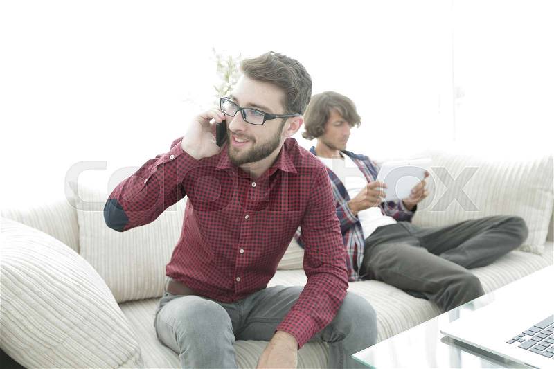 Modern guy talking on smartphone sitting on sofa, stock photo