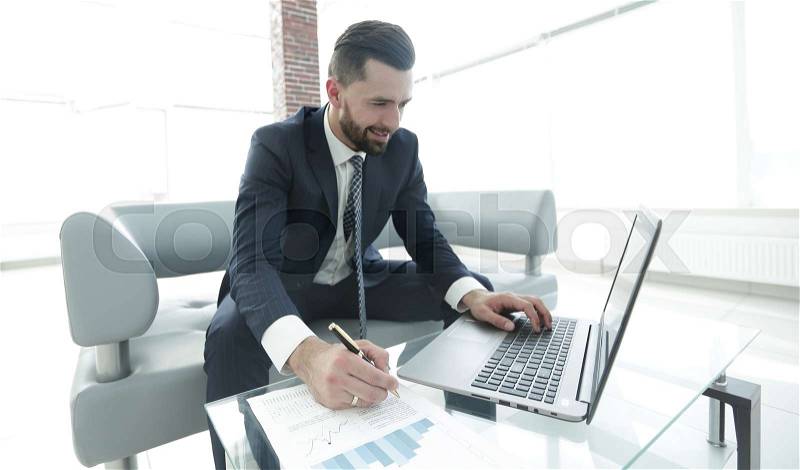 Stylish man working on laptop and making notes in notebook. Photo with copy space, stock photo