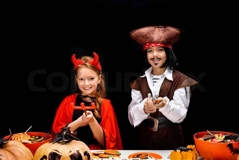 Children in halloween costumes of devil and pirate with halloween decorations and sweets, isolated on black , stock photo