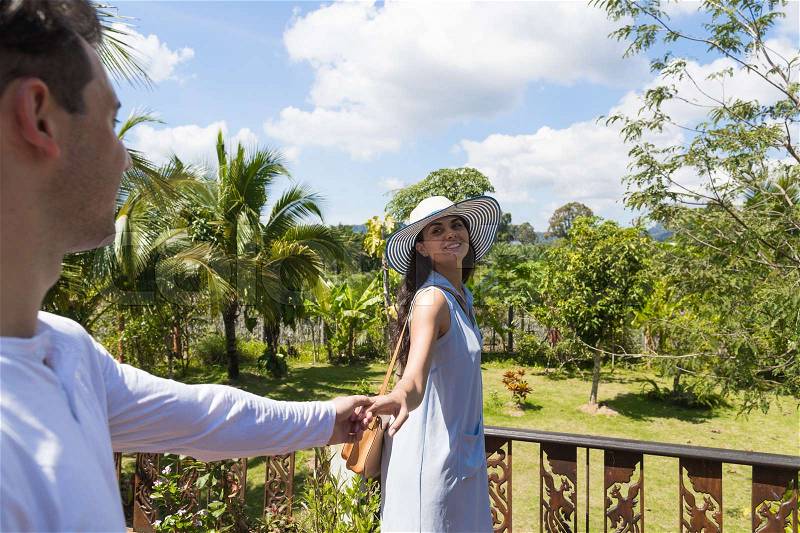 Young Couple On Summer Terrace Or Balcony Cheerful Woman Leading Man To Enjoy Beautiful View Of Tropical Forest, stock photo
