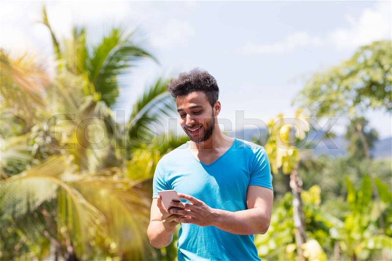 Handsome Latin Man Communicating Online Use Cell Smart Phone Ountdoors Over Tropical Forest And Blue Sky, Portrait Of Young Guy Chatting Social Media Communication Concept, stock photo