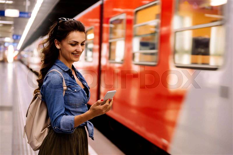 Beautiful woman using her cell phone on subway platform. Transportation Concept, stock photo