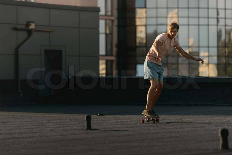 Young man riding on skateboard on rooftop, stock photo