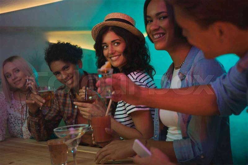Multiethnic group of friends drinking alcohol cocktails together at counter in bar, stock photo