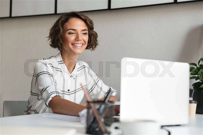Happy woman working by the table with laptop computer, stock photo