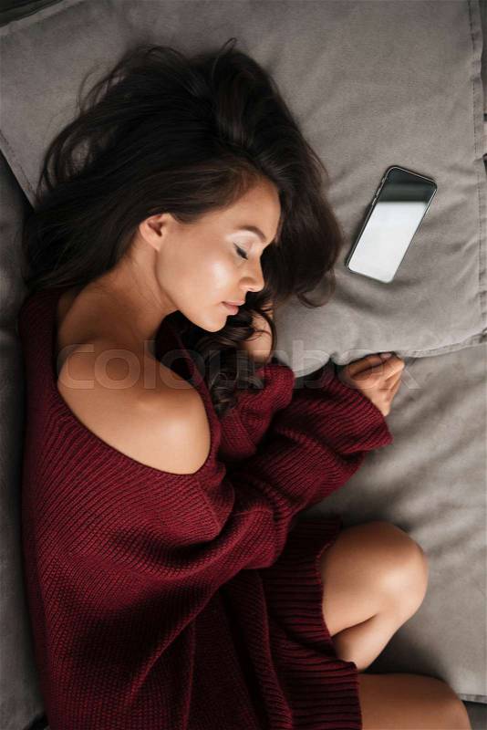 Top view of a beautiful asian woman in sweater sleeping on a couch at home with blank screen mobile phone, stock photo