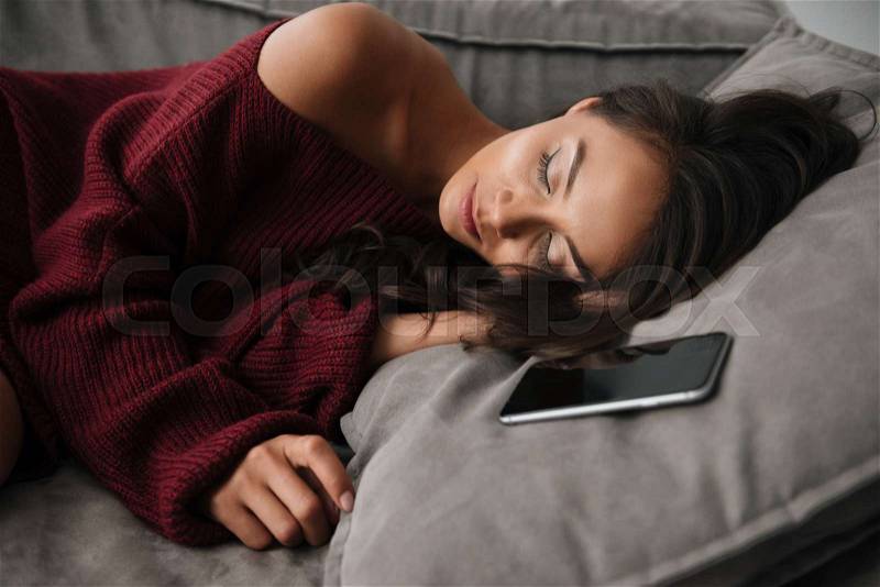 Close up of a beautiful asian woman in sweater sleeping on a couch at home with blank screen mobile phone, stock photo