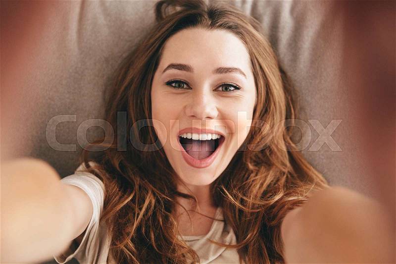 Picture of young amazing happy emotional pretty lady lies on sofa indoors. Looking camera make selfie, stock photo