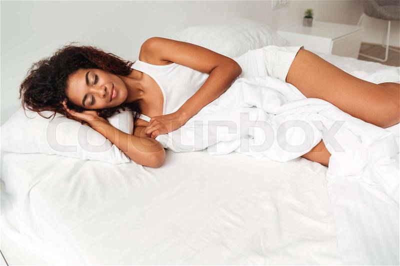 Young calm african woman in pajamas sleeping in bed in the morning, stock photo