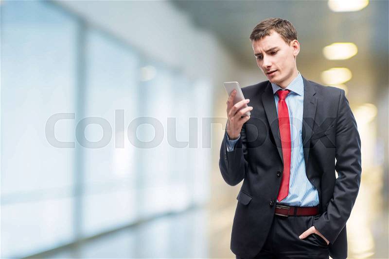 Emotional businessman with phone in hand in office, stock photo