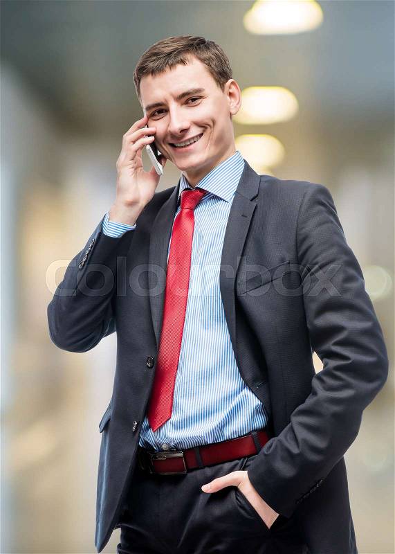 Happy businessman with phone posing in office, stock photo