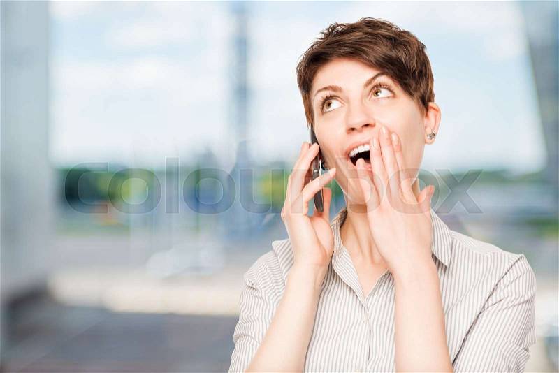 Pleasantly shocked woman with mobile phone in the office, stock photo