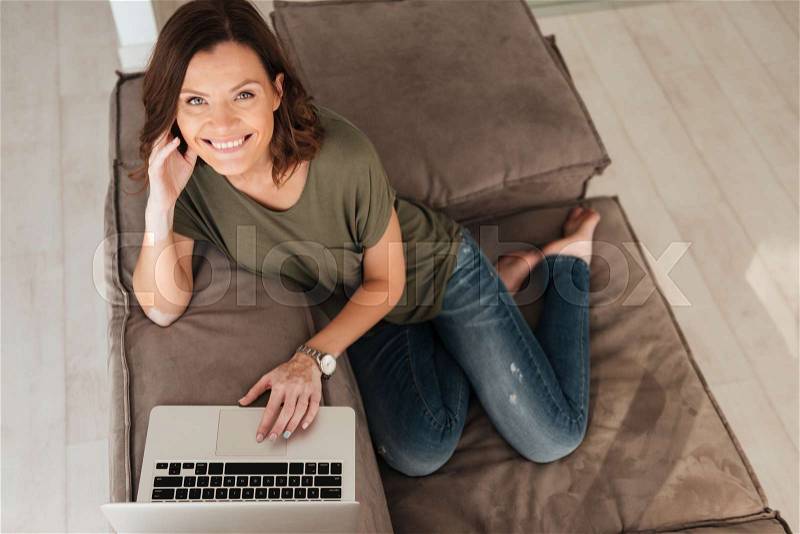 Top view of smiling casual sitting on sofa with laptop computer in home, stock photo