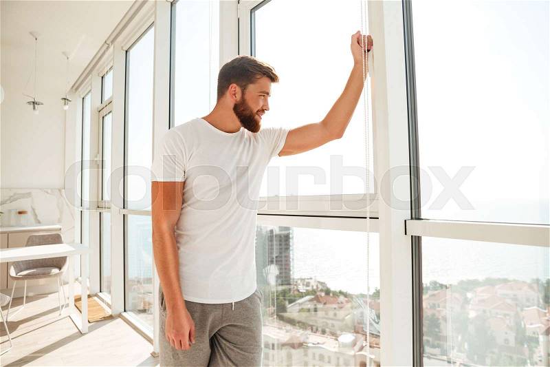 Side view of happy bearded man looking at the window at home, stock photo