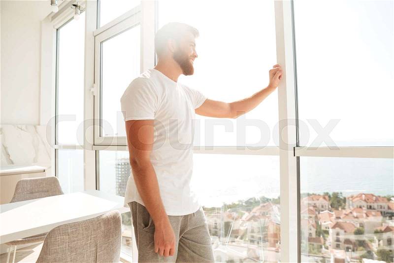 Side view of handsome bearded man looking at the window at home, stock photo