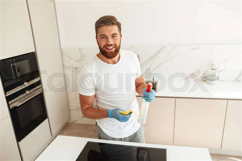 Happy bearded man near the stove with cleaners which looking at the camera, stock photo