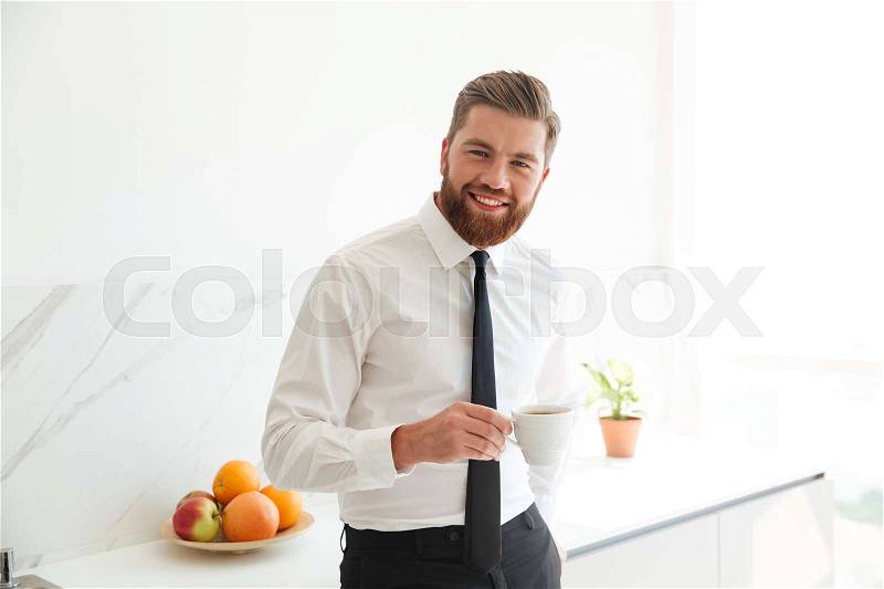 Smiling bearded business man drinking coffee on kitchen and looking at the camera, stock photo