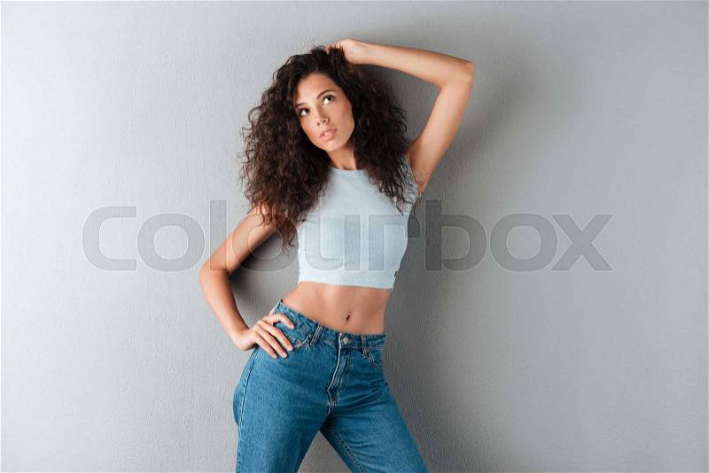 Pensive curly woman posing in studio over gray background, stock photo