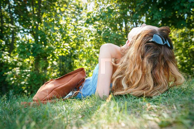 Young woman with a leather backpack lying on a grass in a summer park, stock photo