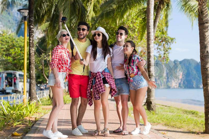 People Group Take Selfie With Action Camera On Stick While Walking In Palm Tree Park On Beach, Happy Smiling Mix Race Friends On Summer Vacation, stock photo