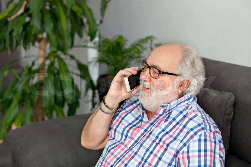 Retired man with white beard and a mobile in his home, stock photo