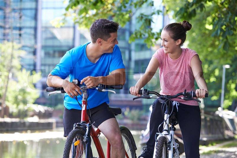 Young Couple Cycling Next To River In Urban Setting, stock photo