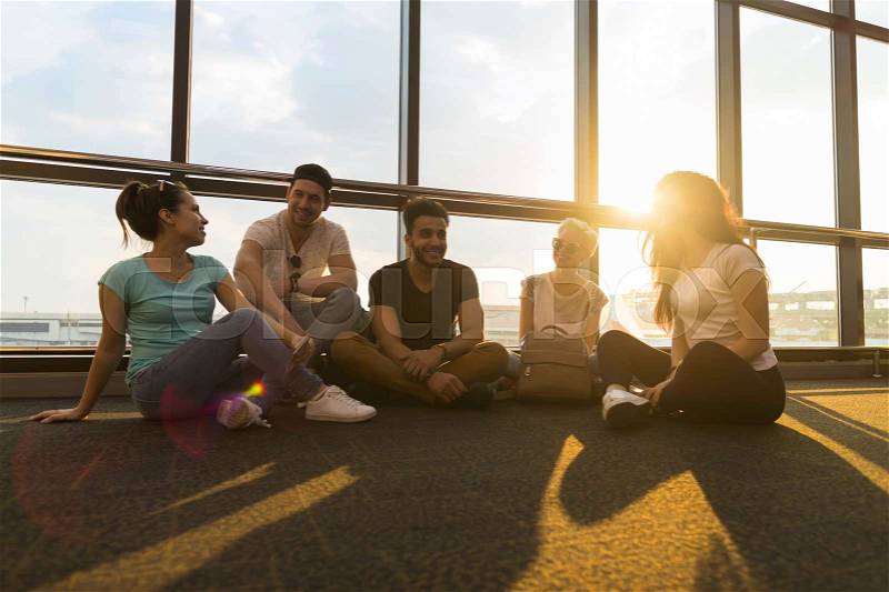 Young People Group Sitting On Floor In Airport Lounge Windows Waiting Departure Speaking Happy Smile Mix Race Friends Flight Delay, stock photo