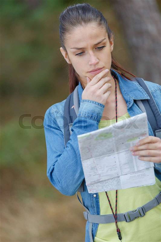 Young woman hiking standing with map in forest, stock photo