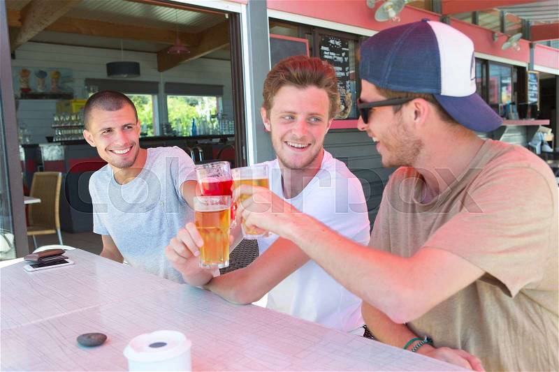 Three male friends relax drinking beer out on restaurant terrace, stock photo