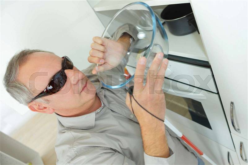 Mature blind man taking a bowl in the kitchen, stock photo
