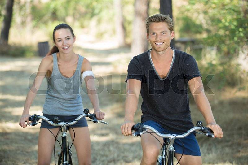 Smiling athletic couple cycling in forest, stock photo