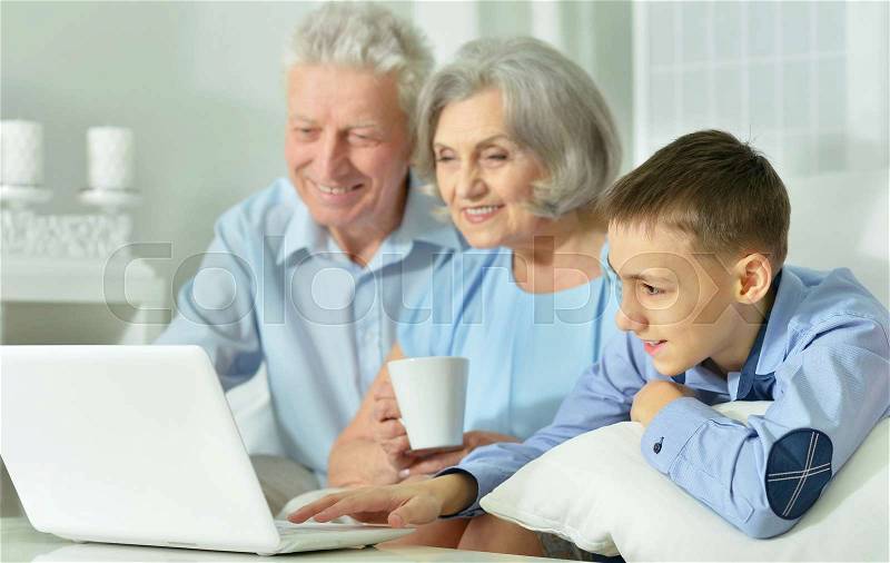 Grandparents and grandson sitting at table and using laptop, stock photo