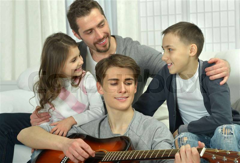 Family listening how boy playing on guitar while sitting on couch, stock photo