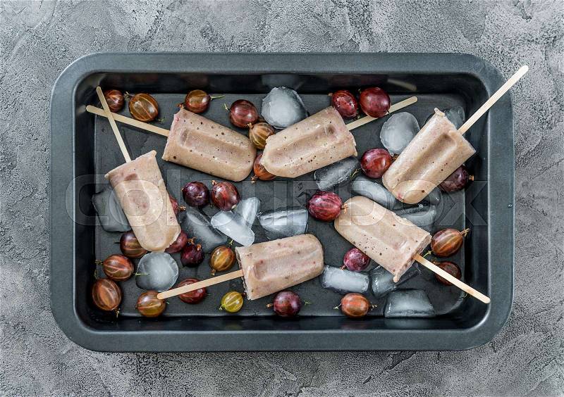 Huge black tray with ice and homemade ice-cream made from gooseberries, on wooden sticks, topview, stock photo