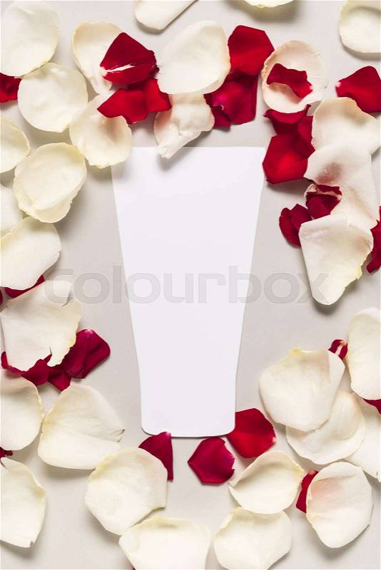 Cut out bottle of lotion on red and white rose petals, isolated on grey, stock photo