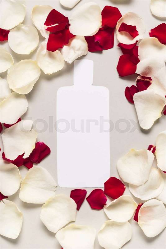 Cut out bottle of lotion on red and white rose petals, isolated on grey, stock photo