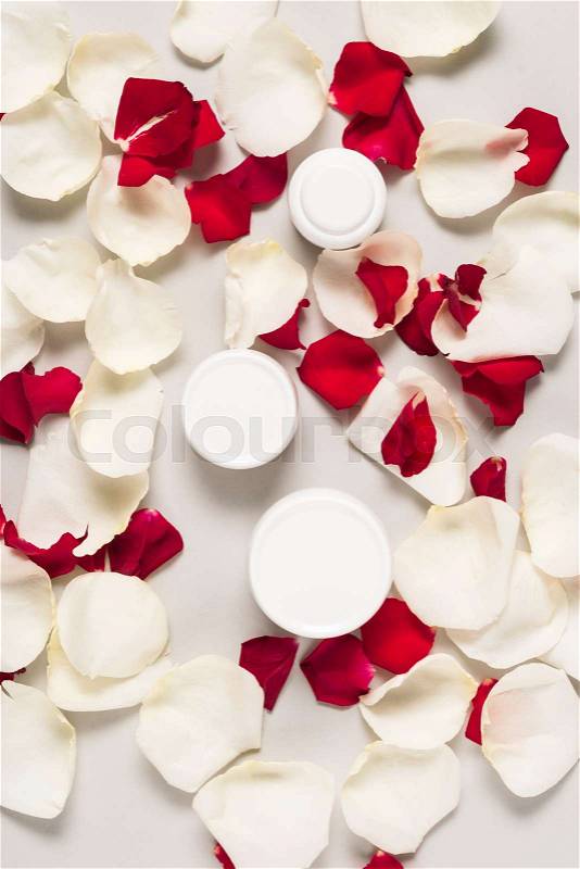 Organic cream in plastic containers on white and red rose petals, isolated on grey, stock photo