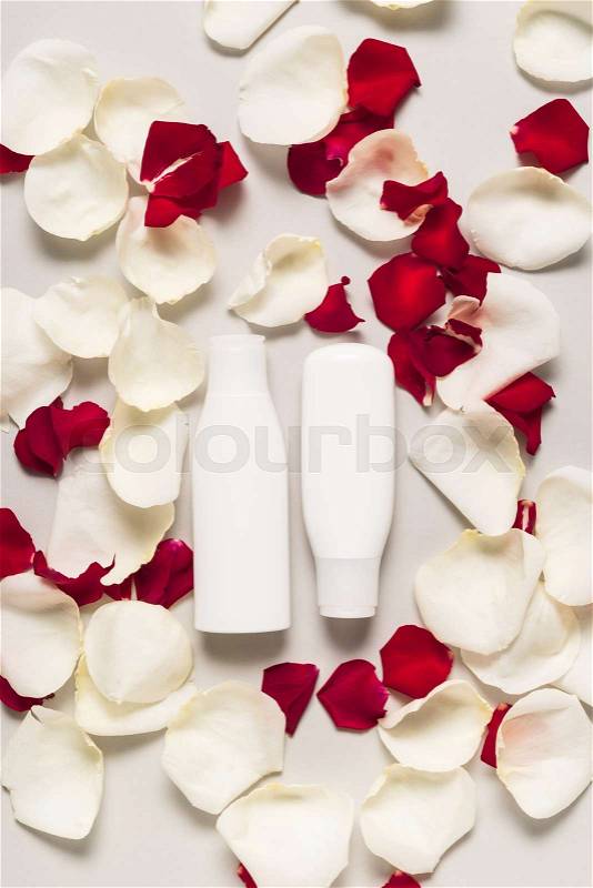 Body lotion in bottles on white and red rose petals, isolated on grey, stock photo