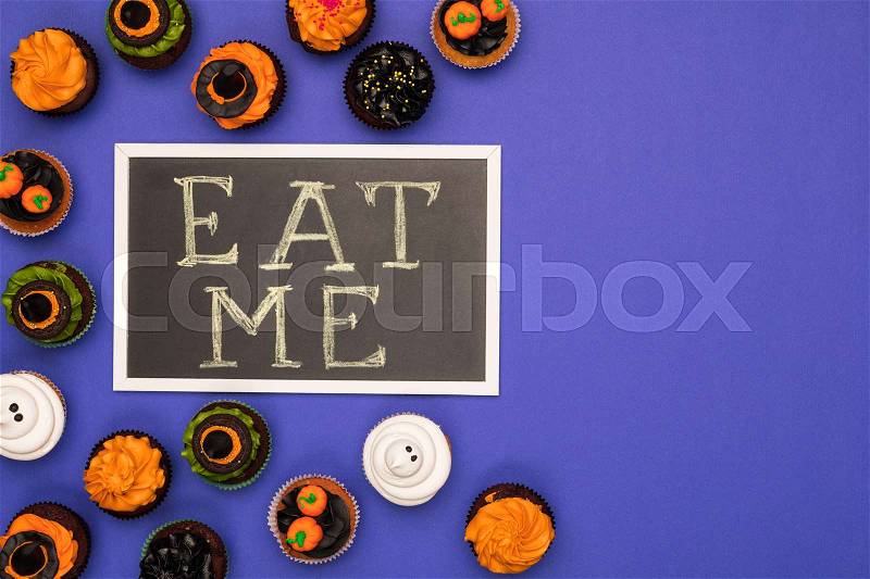 Top view of decorative halloween cupcakes and eat me inscription on blue, stock photo